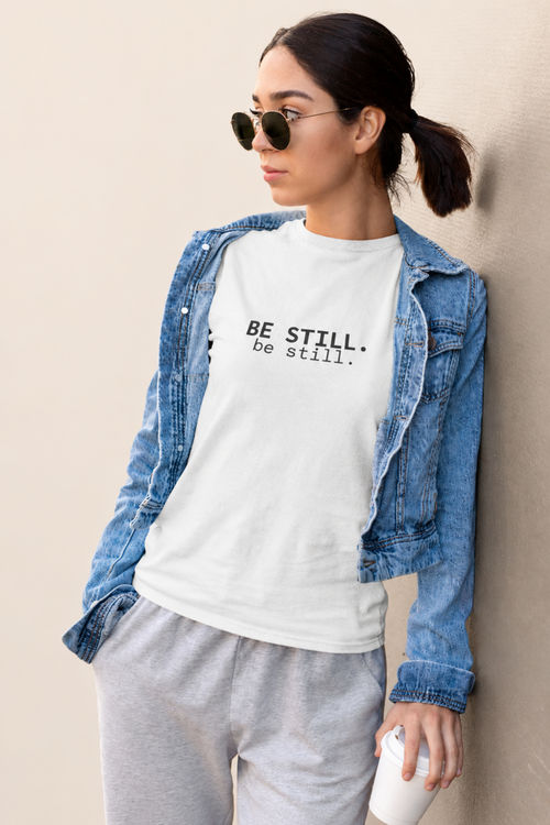 A woman wearing a white graphic t-shirt with the text 'BE STILL. be still.