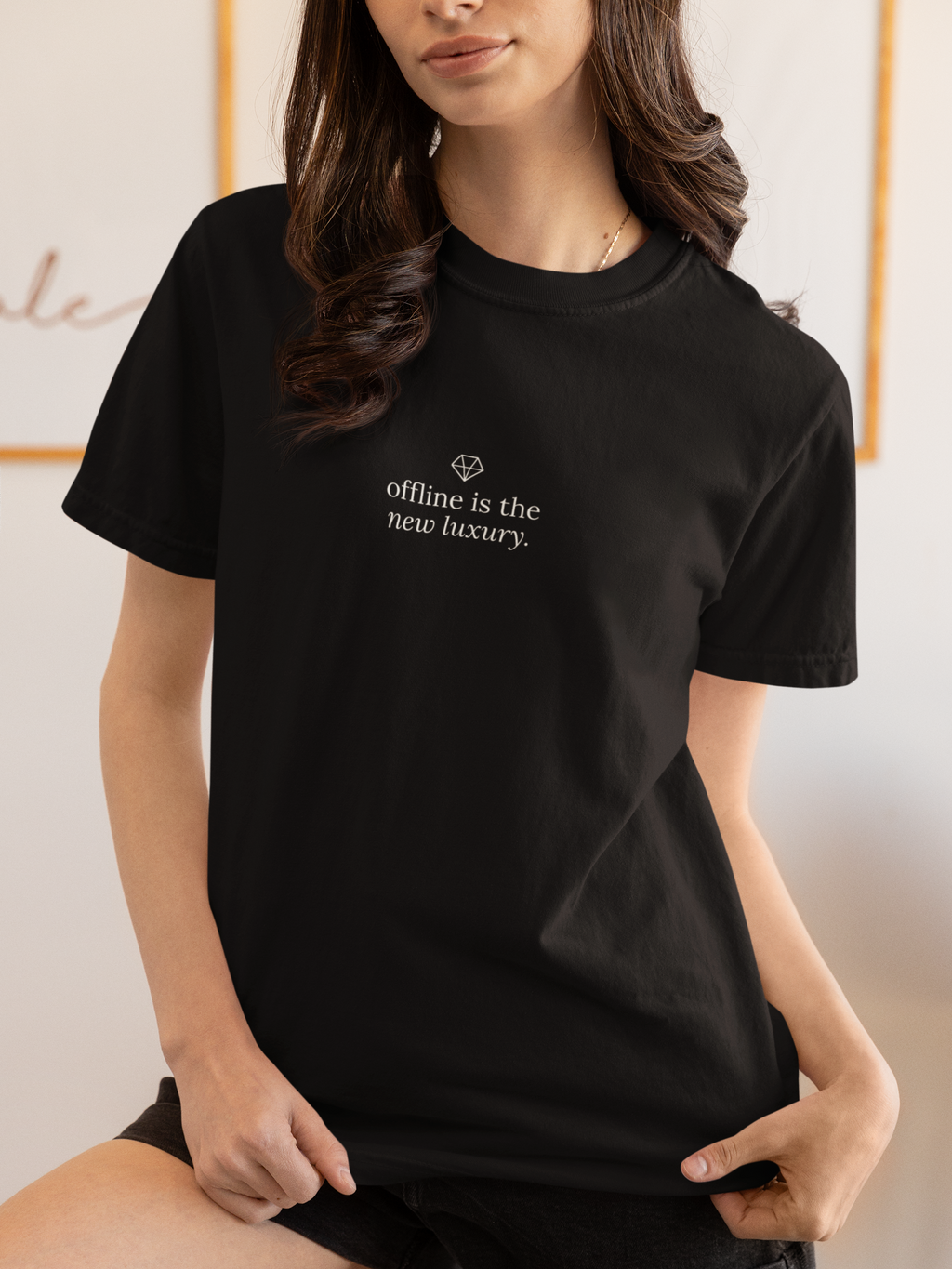 A woman wearing a black short-sleeve crewneck t-shirt with the words 'touch grass.' printed in white across the chest, posed in a brightly lit indoor setting.