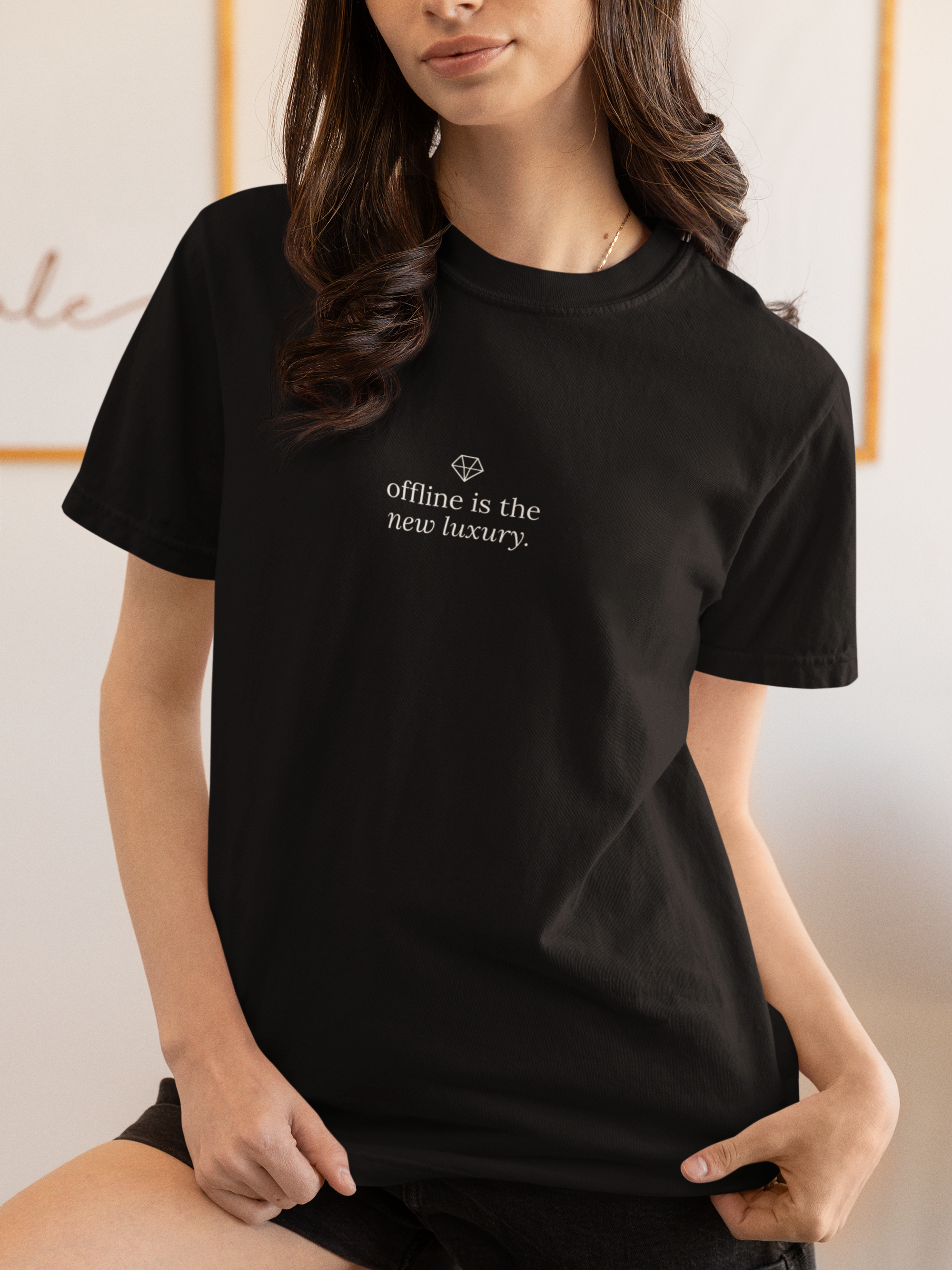 A woman wearing a black short-sleeve crewneck t-shirt with the words 'touch grass.' printed in white across the chest, posed in a brightly lit indoor setting.