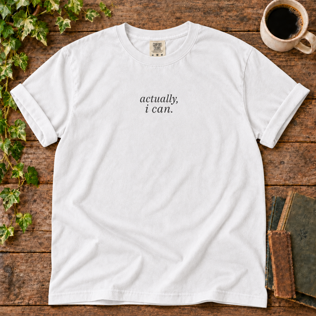 White relaxed-fit tee printed with actually, i can., flat lay on rustic wood with ivy, coffee and vintage books