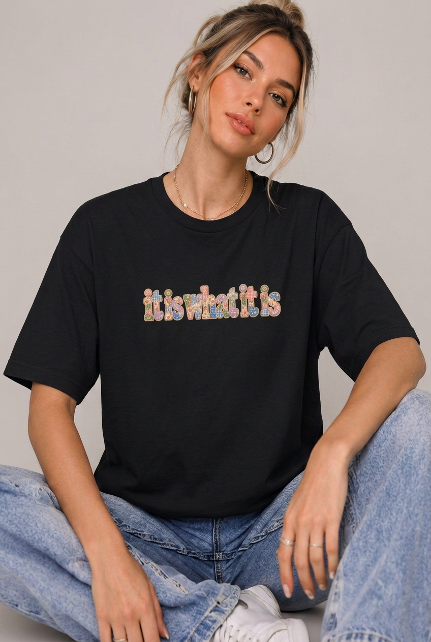 Seated model wearing the it is what it is colourful t-shirt in Black