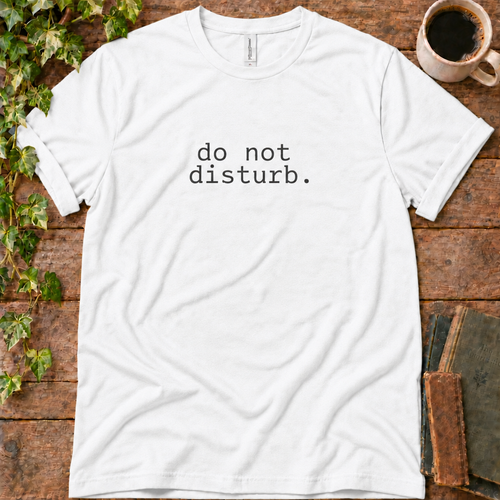 White regular-fit tee printed with do not disturb, flat lay on rustic wood with ivy, coffee and vintage books
