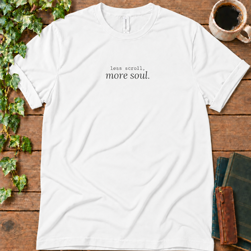 White regular-fit tee printed with less scroll, more soul., flat lay on rustic wood with ivy, coffee and vintage books