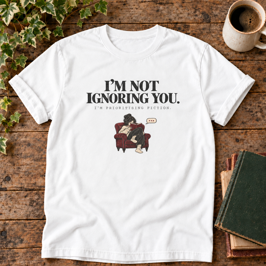 I'm not ignoring you t-shirt in White, flat lay on dark rustic wood with ivy, coffee mug and green-over-red-and-tan book pile