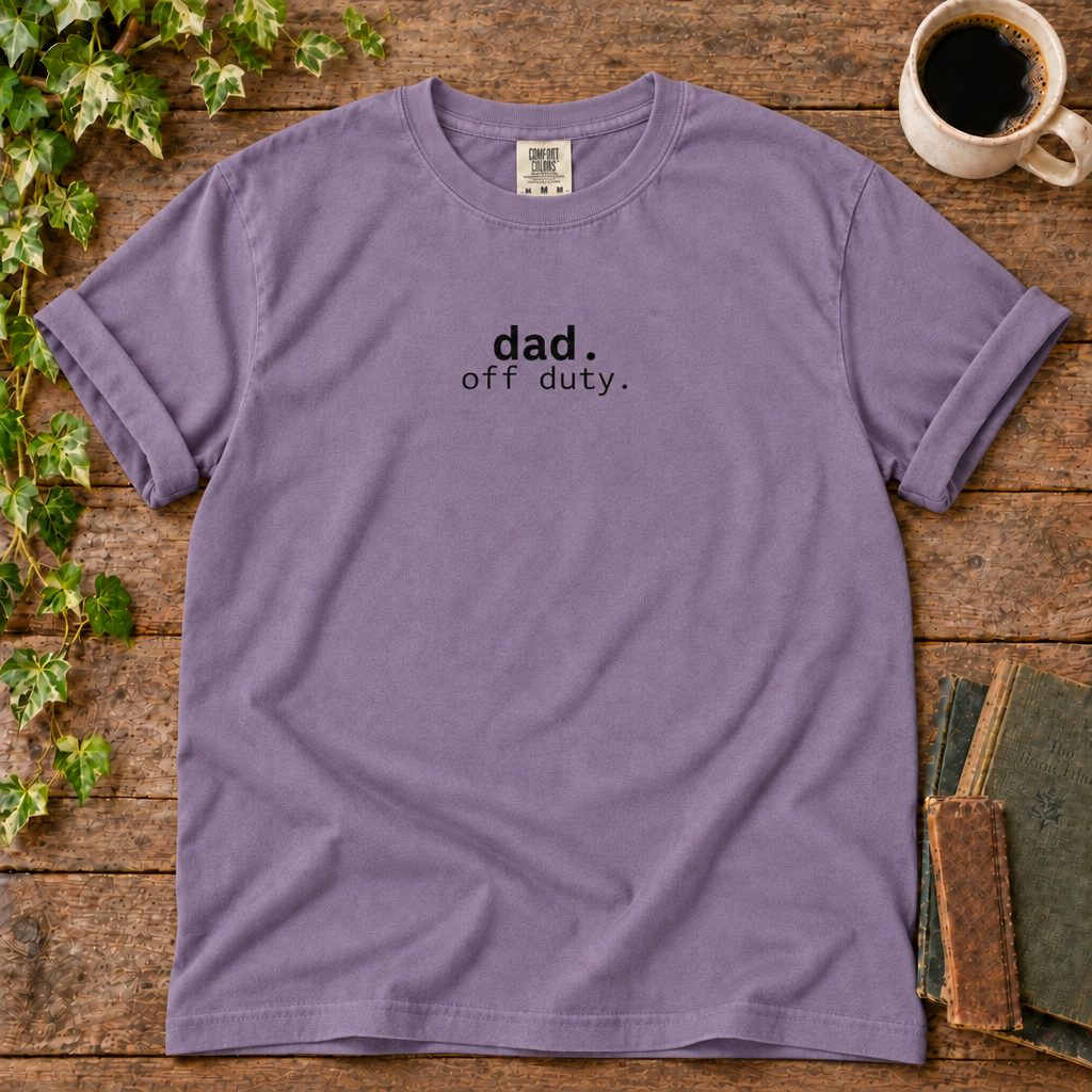 Violet relaxed-fit tee printed with dad off duty, flat lay on rustic wood with ivy, coffee and vintage books