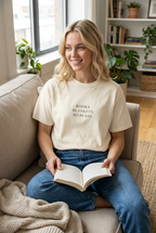 Blonde woman wearing the Ivory books blankets no plans t-shirt while reading on a sofa