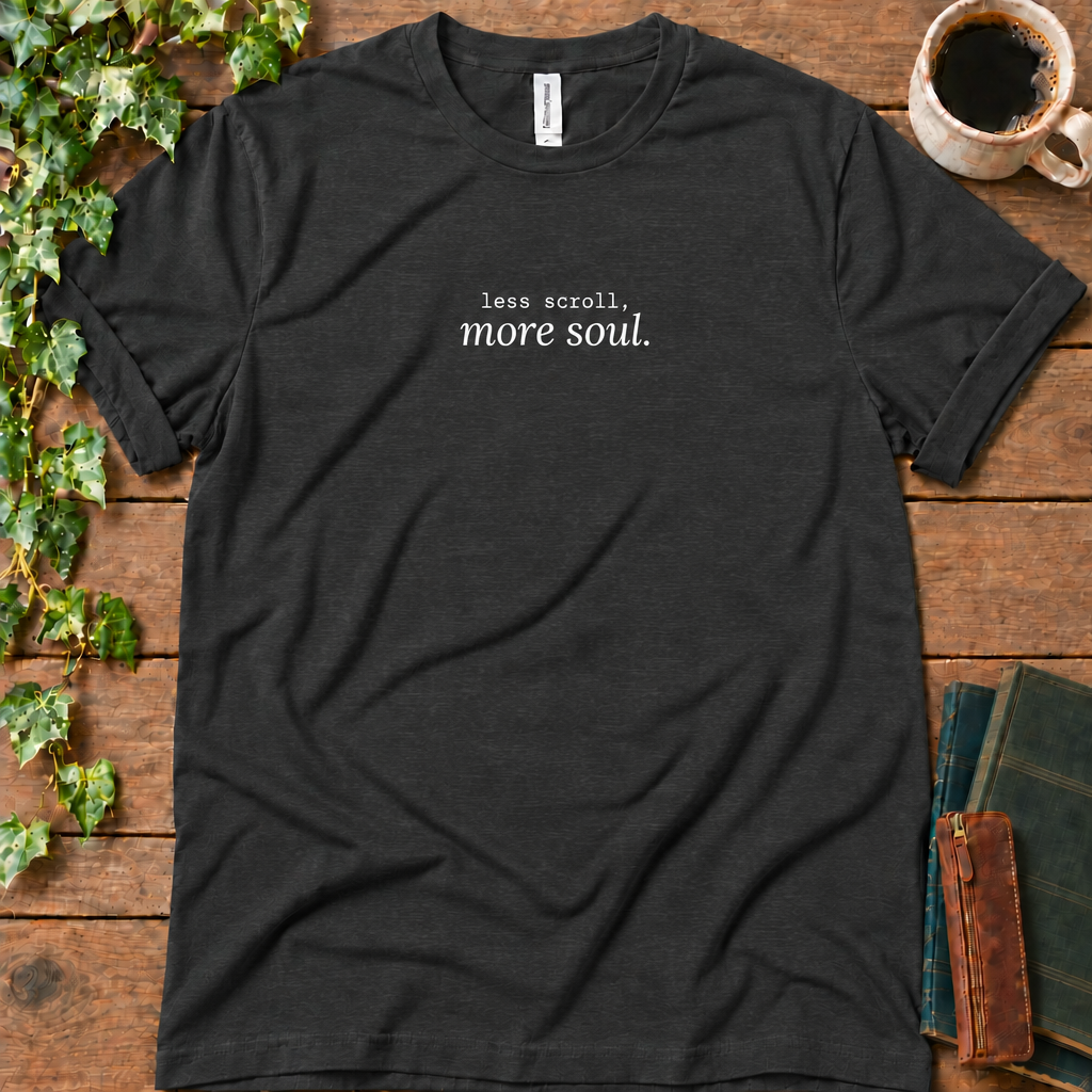 Dark grey heather regular-fit tee printed with less scroll, more soul., flat lay on rustic wood with ivy, coffee and vintage books