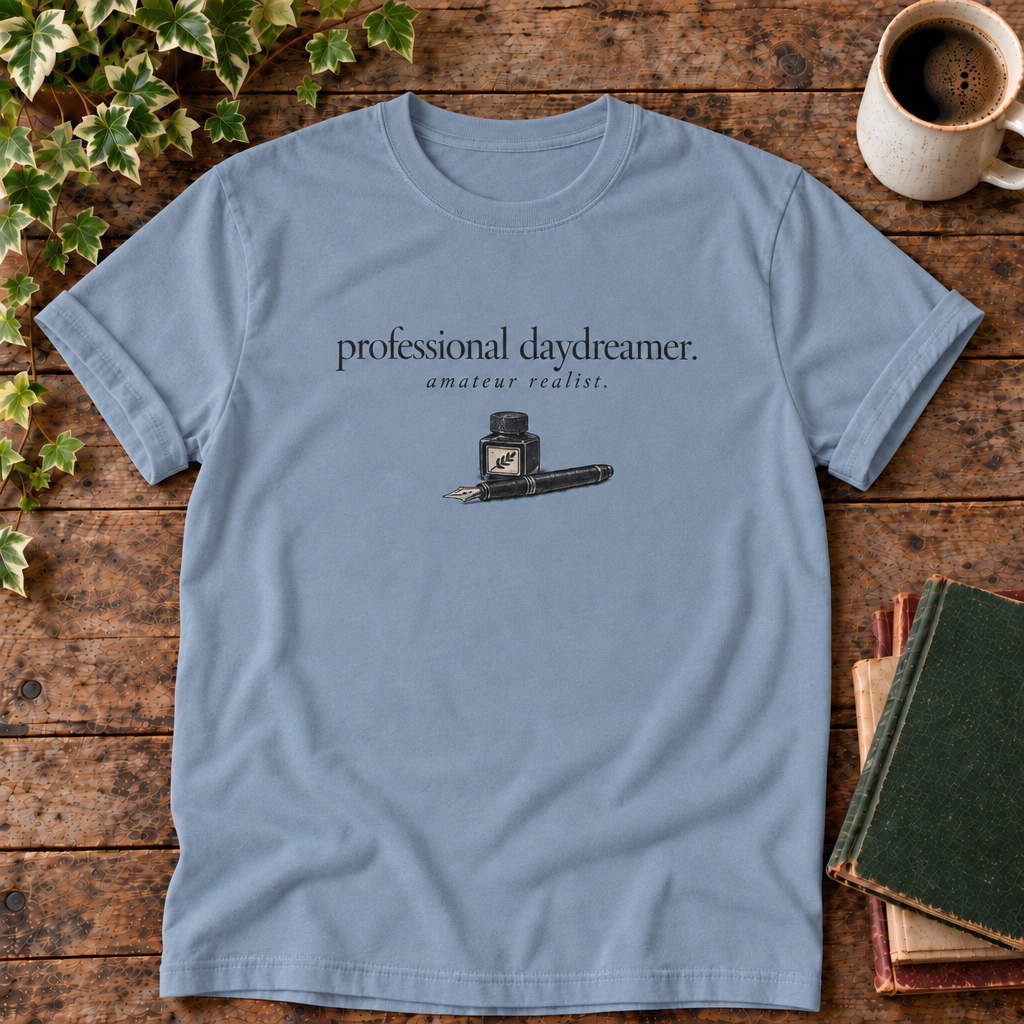 professional daydreamer t-shirt in Blue Jean, flat lay on dark rustic wood with ivy, coffee mug and green-over-red-and-tan book pile