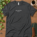 Dark grey heather regular-fit tee printed with my person. always., flat lay on rustic wood with ivy, coffee and vintage books