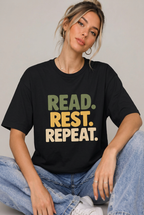 Seated woman wearing the Black read rest repeat t-shirt with blue jeans against a simple studio background