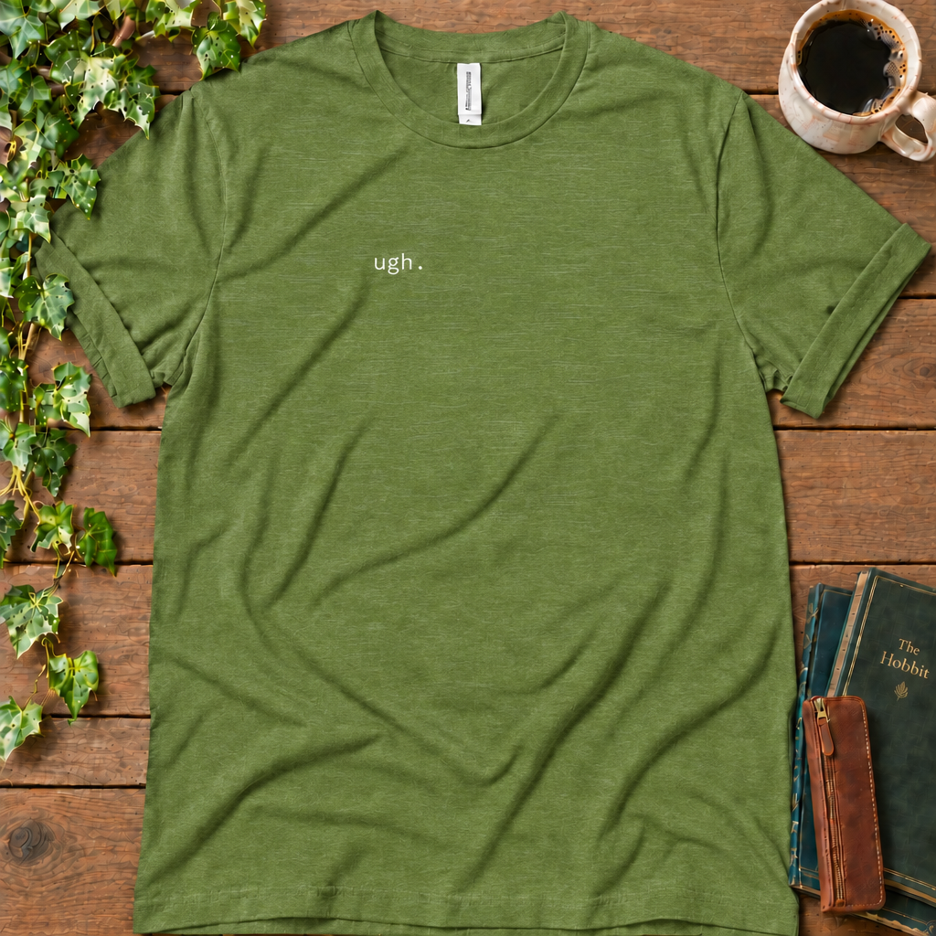 Heather green regular-fit tee printed with ugh. on the left chest, flat lay on rustic wood with ivy, coffee and vintage books