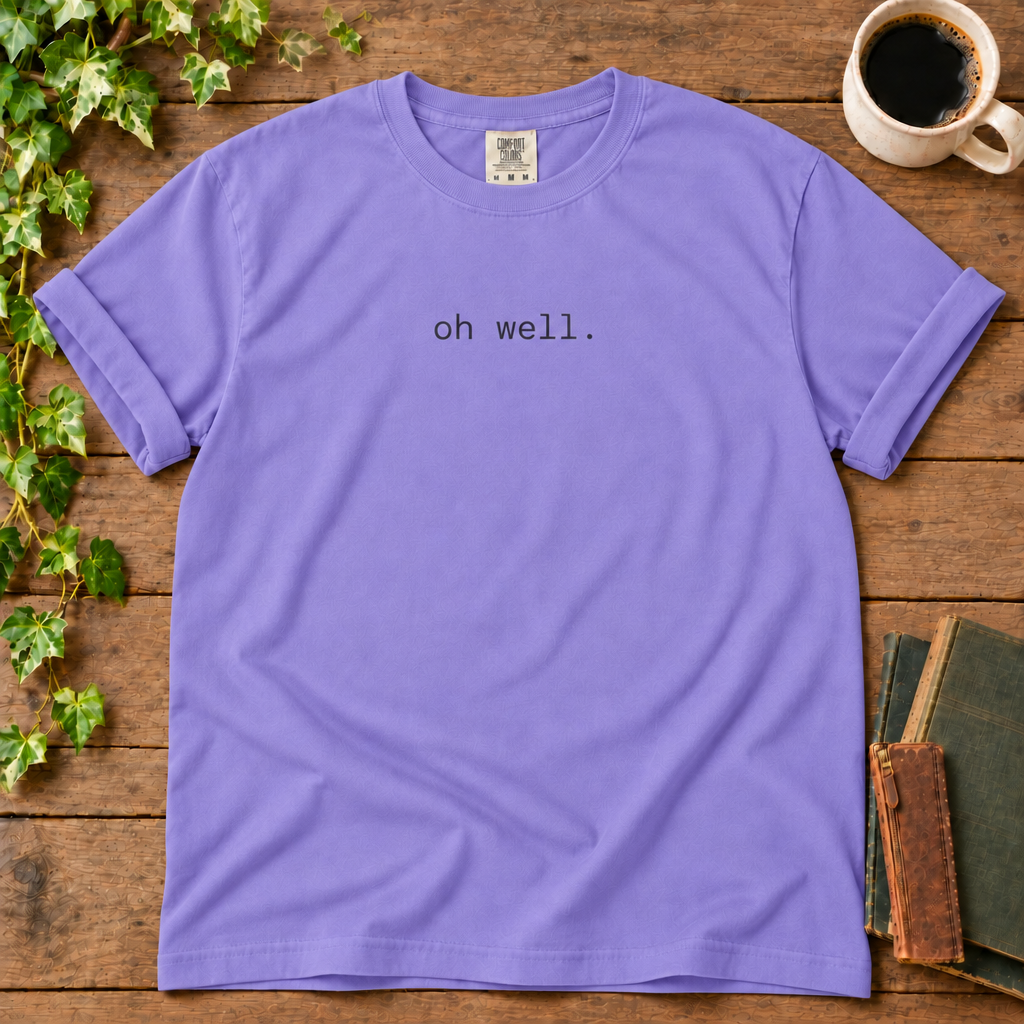 Violet relaxed-fit tee printed with oh well., flat lay on rustic wood with ivy, coffee and vintage books