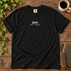 Black relaxed-fit tee printed with dad off duty, flat lay on rustic wood with ivy, coffee and vintage books