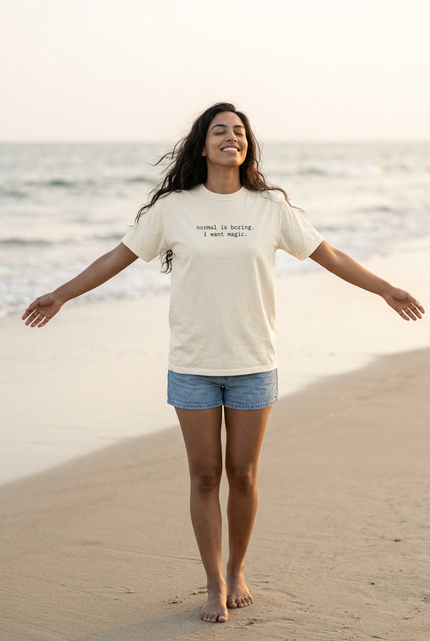 Woman happily spreading her arms on a beach wearing the Ivory normal is boring. i want magic. t-shirt