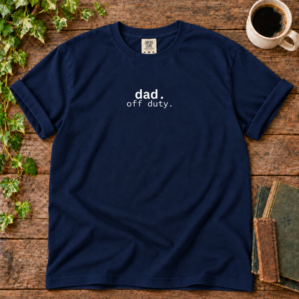 True navy relaxed-fit tee printed with dad off duty, flat lay on rustic wood with ivy, coffee and vintage books