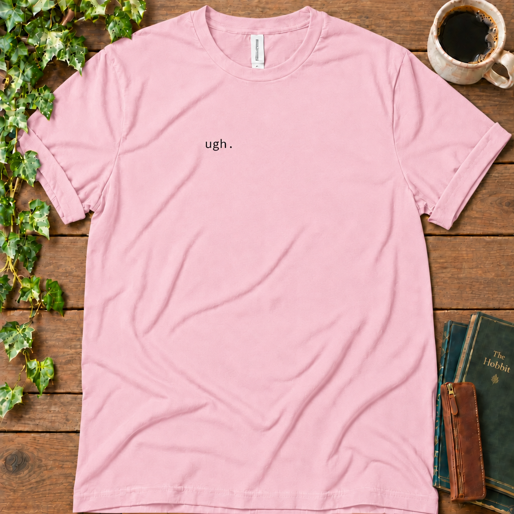 Pink regular-fit tee printed with ugh. on the left chest, flat lay on rustic wood with ivy, coffee and vintage books