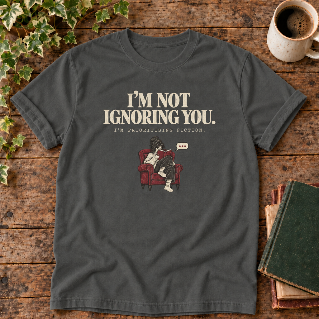 I'm not ignoring you t-shirt in Pepper, flat lay on dark rustic wood with ivy, coffee mug and green-over-red-and-tan book pile, cream ink