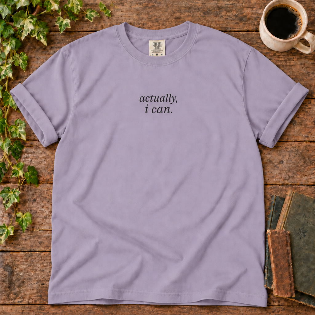 Violet relaxed-fit tee printed with actually, i can., flat lay on rustic wood with ivy, coffee and vintage books