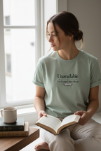 Person wearing the sage Unavailable I've Escaped Into a Book T-shirt while reading by a window