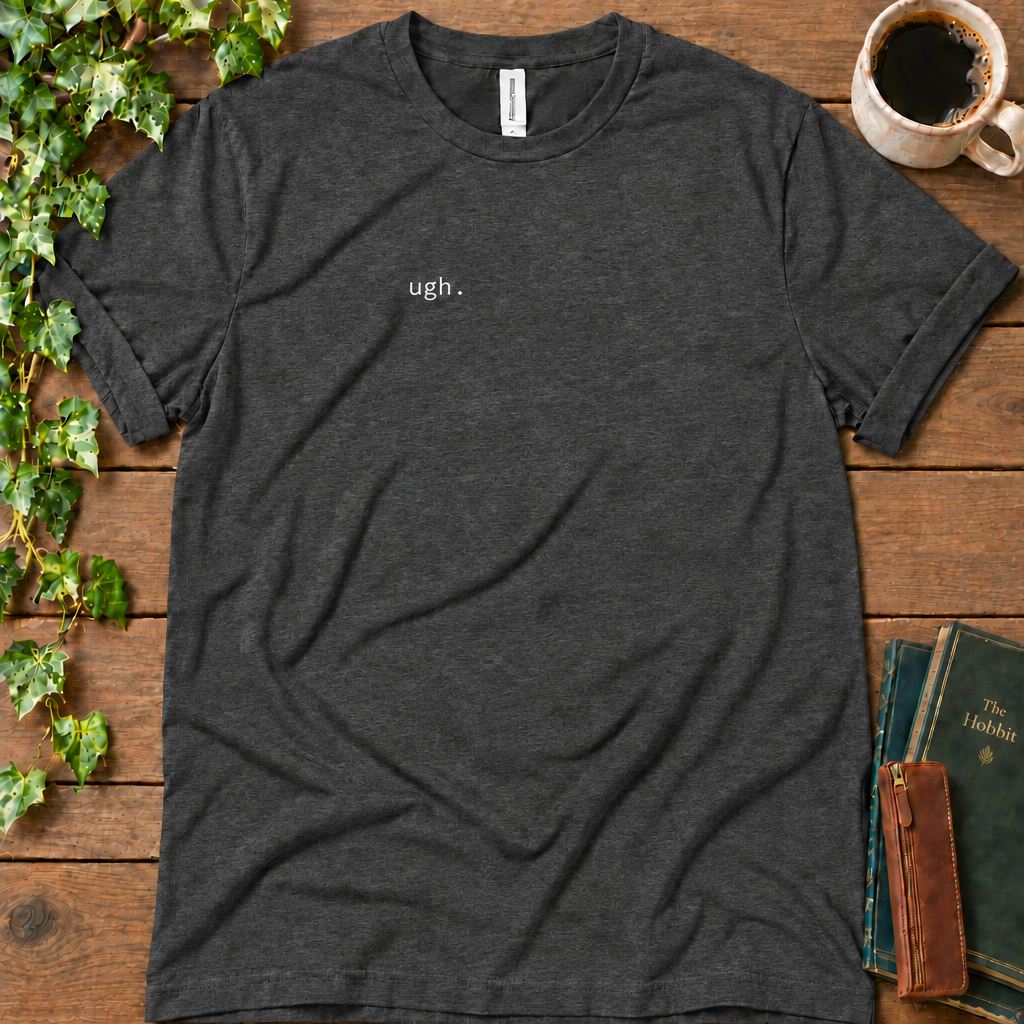 Dark grey heather regular-fit tee printed with ugh. on the left chest, flat lay on rustic wood with ivy, coffee and vintage books