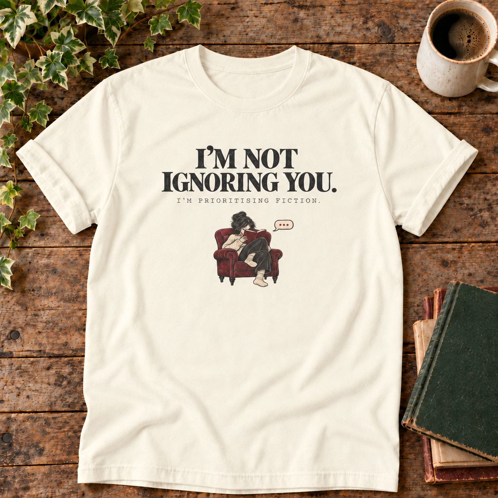 I'm not ignoring you t-shirt in Ivory, flat lay on dark rustic wood with ivy, coffee mug and green-over-red-and-tan book pile
