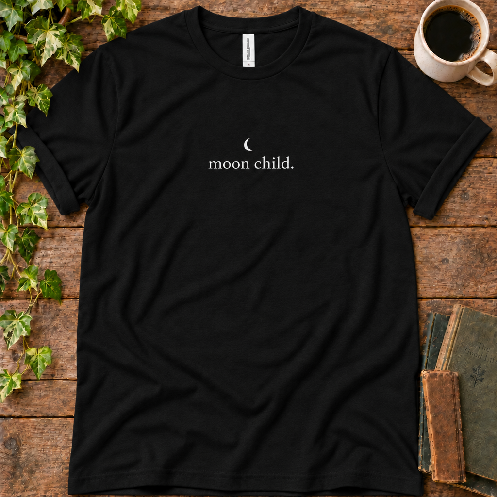 Black regular-fit tee printed with moon child, flat lay on rustic wood with ivy, coffee and vintage books