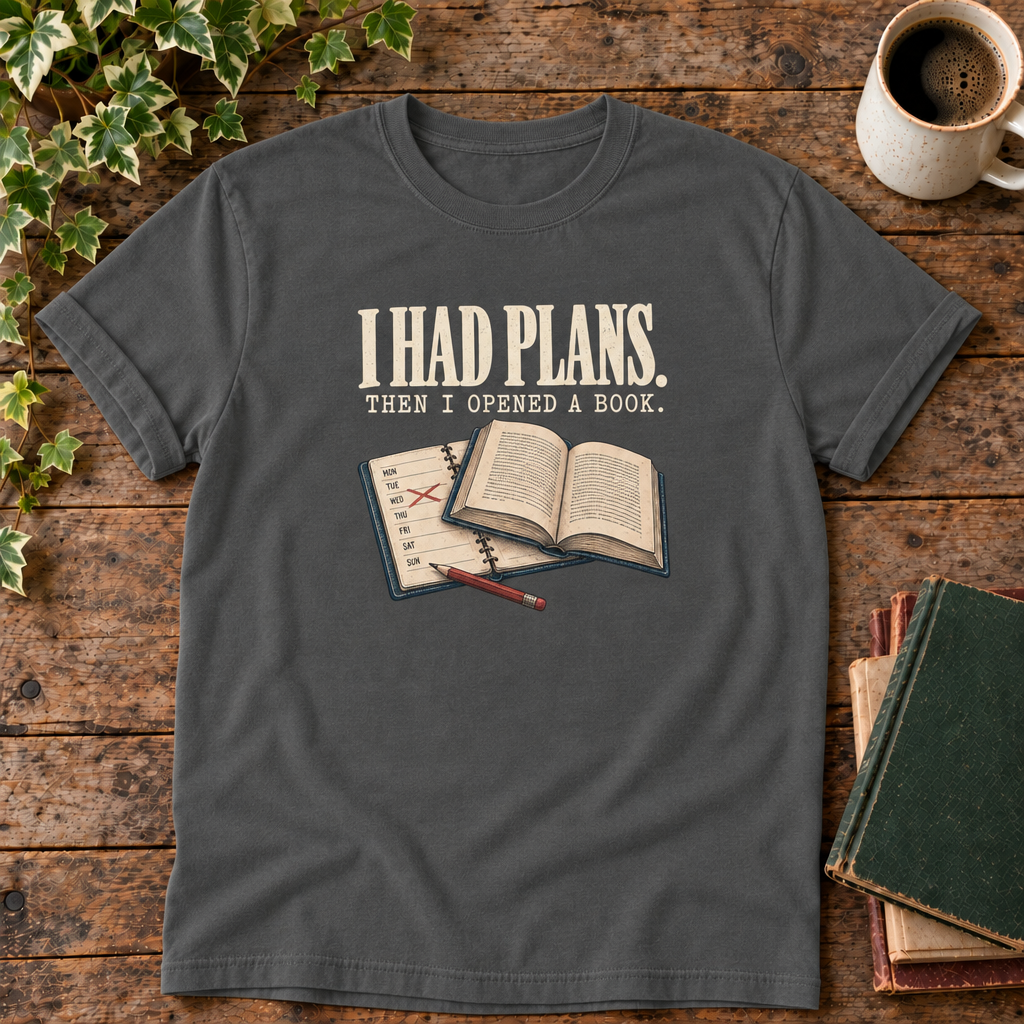 I had plans t-shirt in Pepper, flat lay on dark rustic wood with ivy, coffee mug and green-over-red-and-tan book pile, cream ink