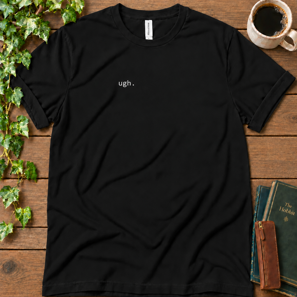 Black regular-fit tee printed with ugh. on the left chest, flat lay on rustic wood with ivy, coffee and vintage books