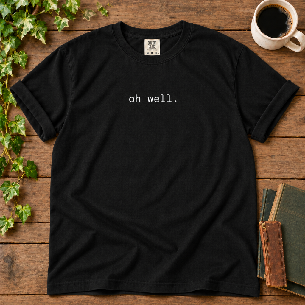 Black relaxed-fit tee printed with oh well., flat lay on rustic wood with ivy, coffee and vintage books