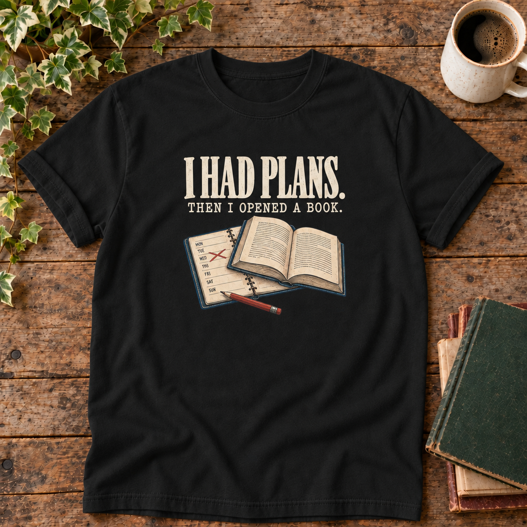 I had plans t-shirt in Black, flat lay on dark rustic wood with ivy, coffee mug and green-over-red-and-tan book pile, cream ink