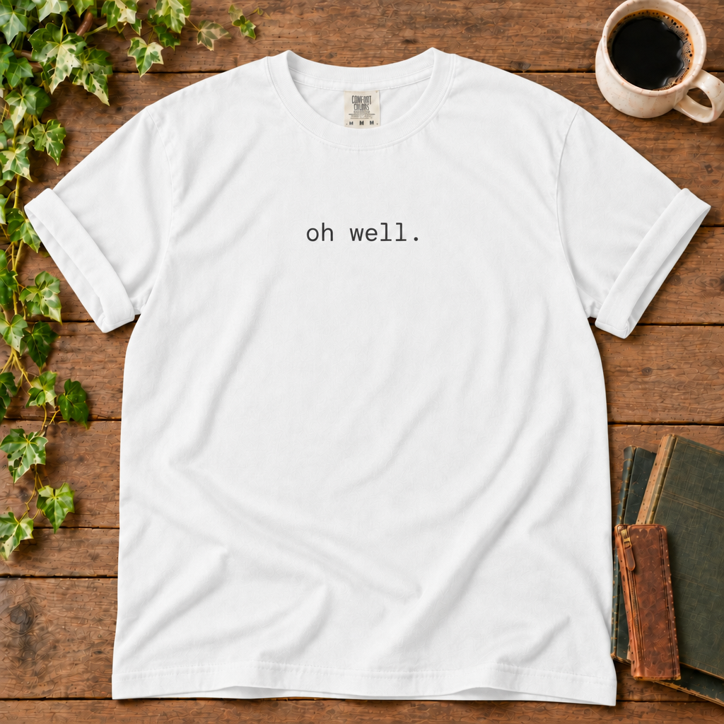 White relaxed-fit tee printed with oh well., flat lay on rustic wood with ivy, coffee and vintage books